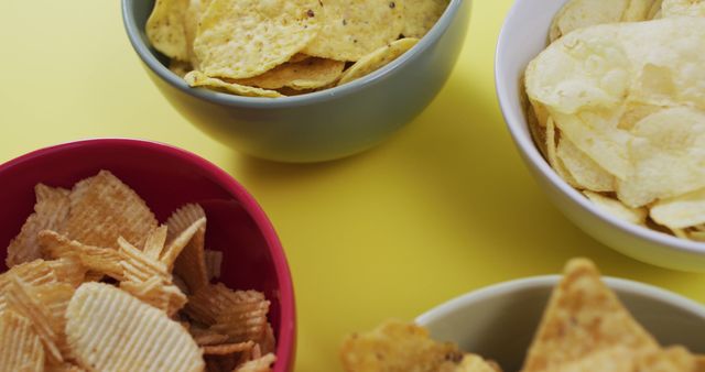 Close up of four bowls full of variety of chips on yellow surface. food and snack concept