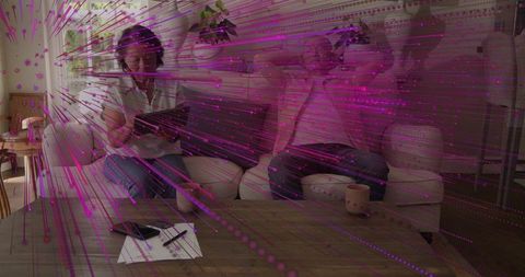 Couple using tablets on sofa with purple digital data overlay in cozy sunlit living room