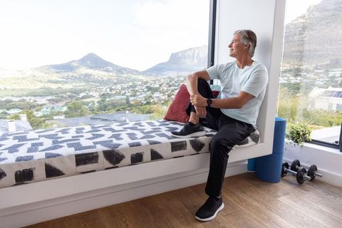 Mature man on window bench overlooking panoramic mountain town from minimalist home gym