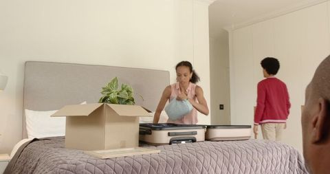Woman Organizing Suitcase on Bed While Man Walking in Bedroom