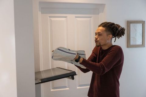 Man removing baking tray from wall oven wearing striped oven mitts in contemporary kitchen