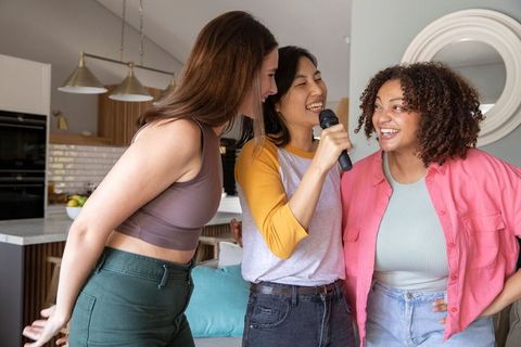 Diverse trio singing karaoke, living room fun and friendship
