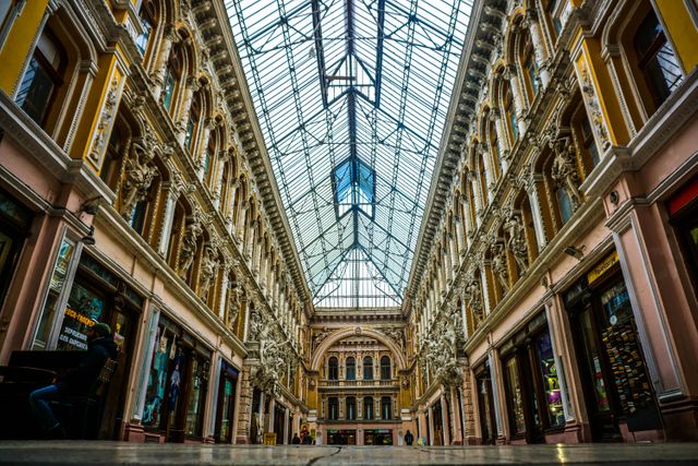 Elegant historic shopping gallery featuring ornate architecture with detailed cornices and a glass roof. Ideal for use in travel blogs, tourism promotion materials, interior design showcases, and advertisements related to luxurious shopping experiences.