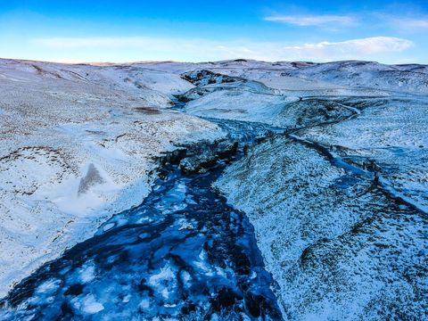 Aerial frozen river valley carving through snow-covered winter highlands at blue hour