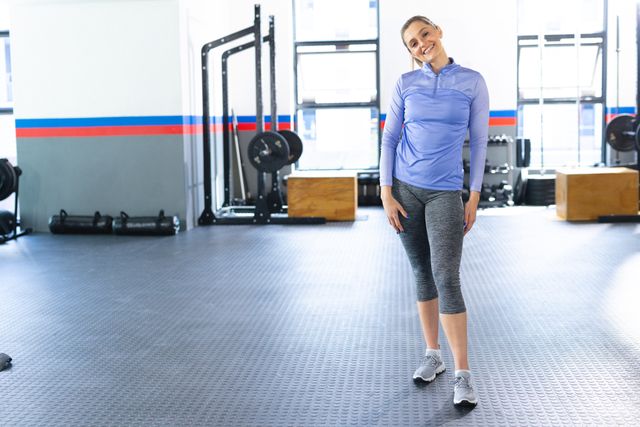 Happy fit woman exercising in a modern gym. Ideal for promoting fitness, health, and active lifestyle content. Suitable for use in advertisements, fitness blogs, and social media posts about workout routines and gym environments.