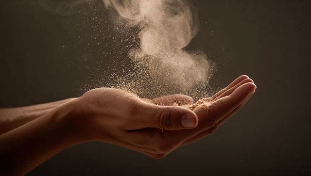 Cupped hands releasing fine dust plume with floating particles and warm light