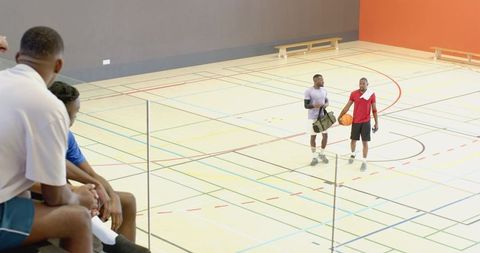 African american teammates dribbling basketball on indoor court greeting friends on stands