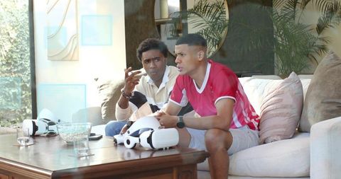 Two friends gaming with vr headsets on sunlit cozy contemporary living room couch