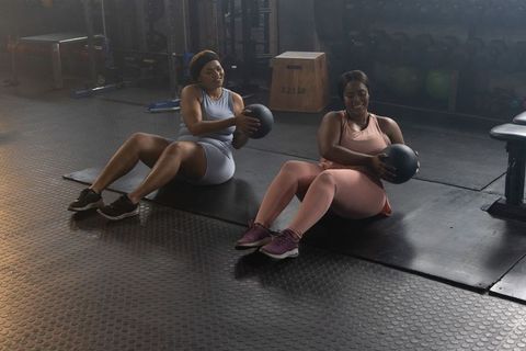 African american women performing russian twists with medicine balls on gym mats
