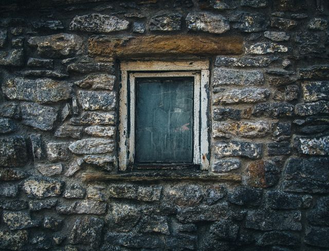Rustic stone wall with a weathered window frame, depicting an old and vintage architectural style. Suitable for concepts related to history, architecture, rustic living, or construction. Can be used for backgrounds, textures, or in illustrating historical architecture.