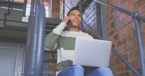 Young Man Balancing Laptop and Phone in Loft Office