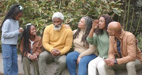 Multigenerational family sitting on bench in garden wearing knit sweaters holding white flowers