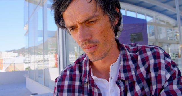 Pensive Man in Checkered Shirt Gazing Downwards Inside Modern Building - Download Free Stock Images Pikwizard.com