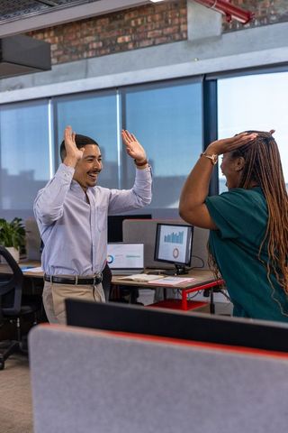 Diverse coworkers celebrating success with high-fives in modern office