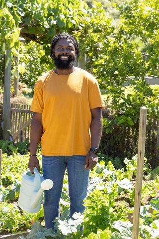 African gardener smiling holding watering can in sunny vegetable garden