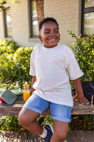 Smiling african american boy sitting on bench outdoors with lunchbox and juice