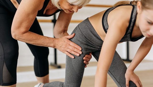 Senior trainer guiding young student through lunge and hip alignment in barre class