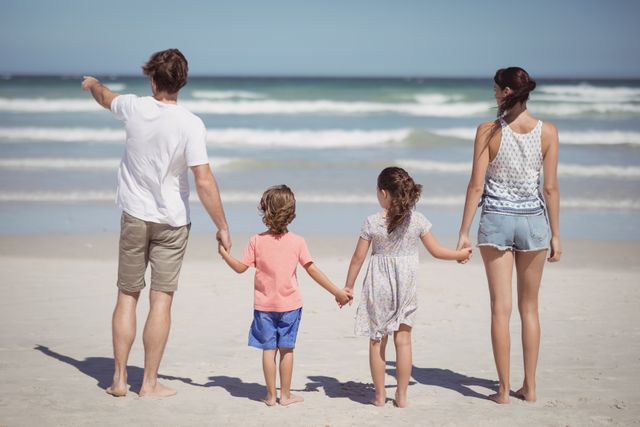 Rear view of man pointing away while standing with family at beach during sunny day