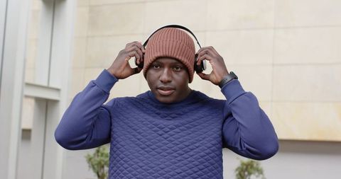 African American Man Adjusting Headphones Wearing Beanie and Smartwatch in Courtyard