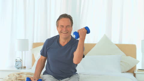 Senior Man Exercising with Dumbbells on Bed at Home