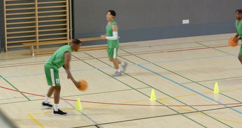 Diverse male basketball players dribbling cones in indoor gym agility training drill