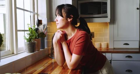 Asian woman contemplating at kitchen window in natural light