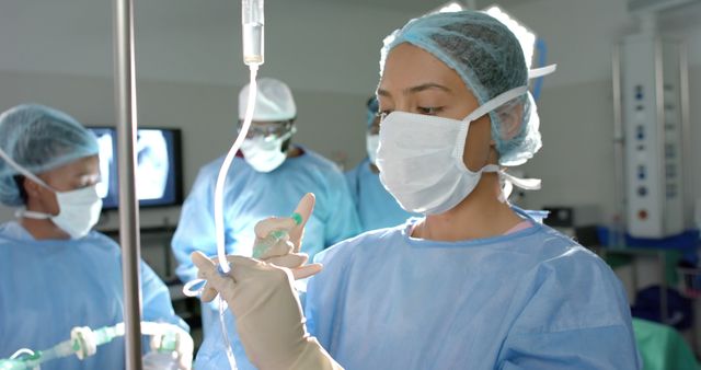 Diverse surgeons with face masks checking drip during surgery in operating room. Medicine, healthcare, surgery and hospital, unaltered.
