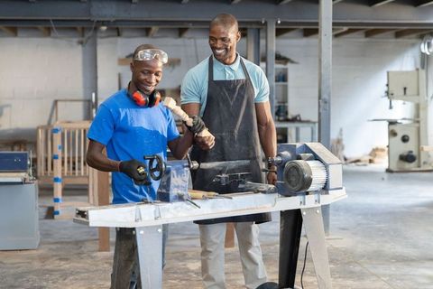 African american men learning woodturning and operating lathe in workshop apprenticeship