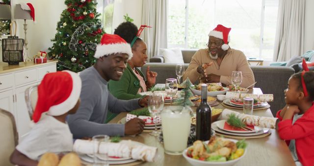 Family members, wearing Santa hats, gathering around a dining table, sharing a joyful Christmas dinner. The room is decorated with a Christmas tree and festive decor. Perfect for use in holiday promotion materials, greeting cards, and advertisements depicting family togetherness during the Christmas season.