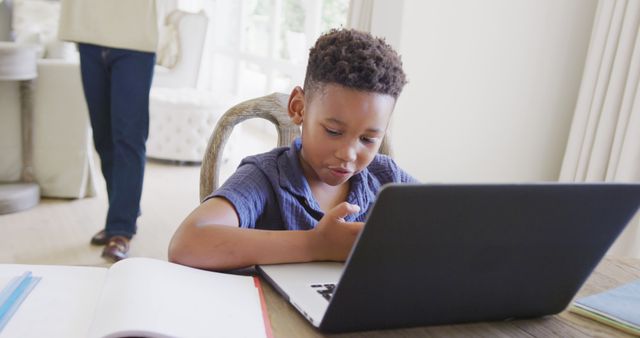 Boy engaging in an online class using a laptop in a bright, well-lit room, with an open notebook on the table. Great for themes of modern education, homeschooling, remote learning, online schooling, and childhood tech engagement.
