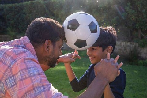 Father and Son Balancing Soccer Ball Outdoors During Playful Bonding