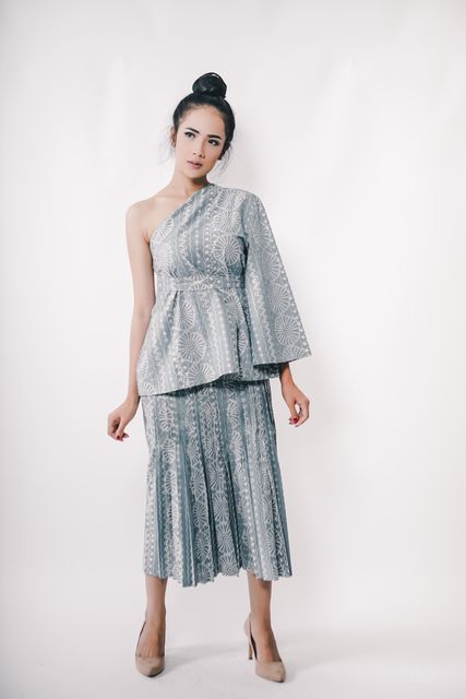 Elegant young woman standing confidently in traditional one-shoulder dress with intricate pattern. Ideal for fashion magazines, cultural representation, and style blogs. Suitable for articles on traditional attire, modern fashion fusion, and empowering women.