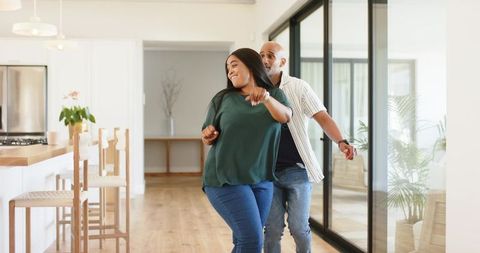 African american couple walking joyfully through sunlit modern open-plan home
