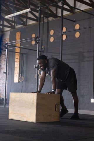 African american athlete leaning on plyo box after intense workout in industrial gym