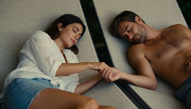 Couple reclining holding hands on poolside lounge chairs relaxing together