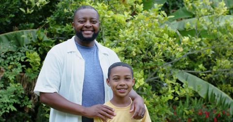 Smiling african american father embracing son in lush backyard garden showing wedding ring