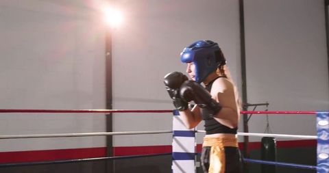 Female Boxer Standing in Ring Corner Wearing Blue Headguard and Black Gloves Sparring