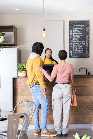 Couple ordering coffee at counter with barista in modern cafe with chalkboard menu