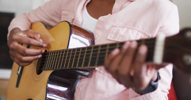 Close-up of person playing acoustic guitar at home. This image shows a casual and relaxing moment, ideal for promoting music lessons, hobby activities, and lifestyle content related to music and relaxation.