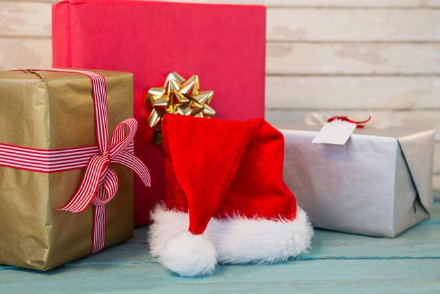 Christmas gifts wrapped in various colors and patterns, accompanied by a Santa hat, placed on a wooden table. Ideal for holiday marketing, festive promotions, greeting cards, or blog posts about Christmas celebrations and gift-giving.