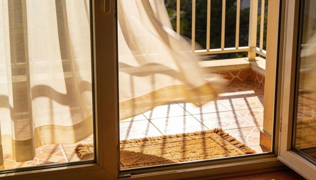 Billowing Sheer Curtain and Open Sliding Door to Sunlit Balcony with Coir Mat and Shadows