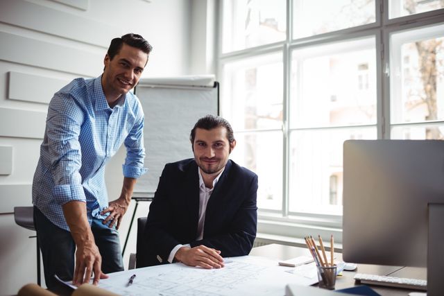 Portrait of smiling interior designer with coworker working on blueprint in office