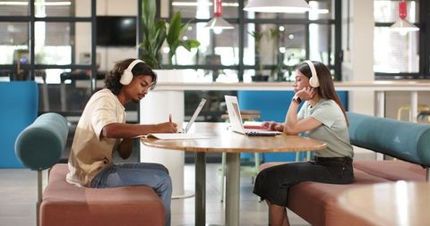 Young adults studying and working with laptops and headphones in modern coworking lounge