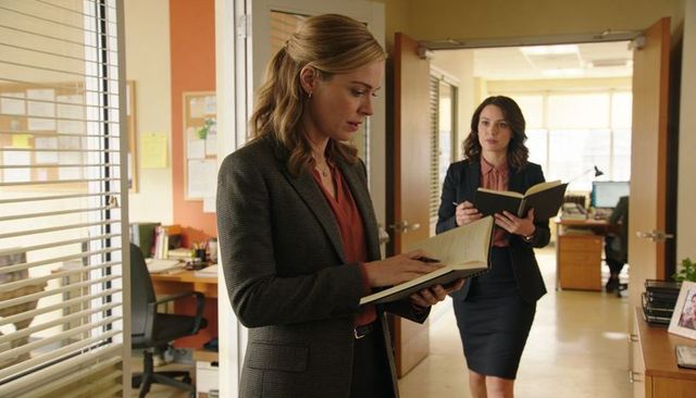 Two businesswomen collaborating in office corridor holding notebooks and planning tasks