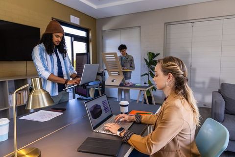 Multicultural team collaborating in modern coworking space woman typing on laptop