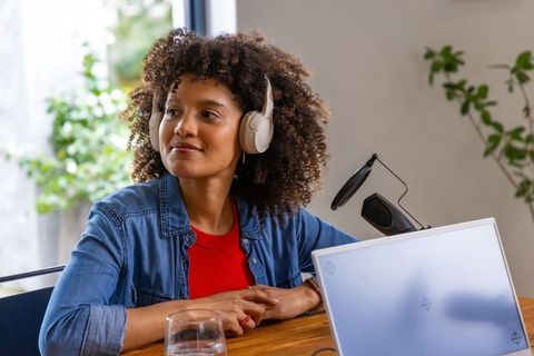 African american woman recording podcast in home studio with headphones and laptop