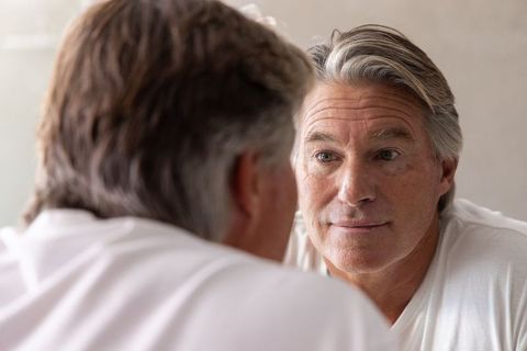Mature man reflecting in mirror, contemplating life in soft natural light