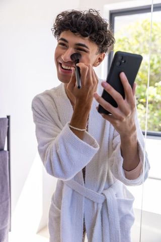 Man Applying Makeup in Bathroom Using Smartphone as Mirror