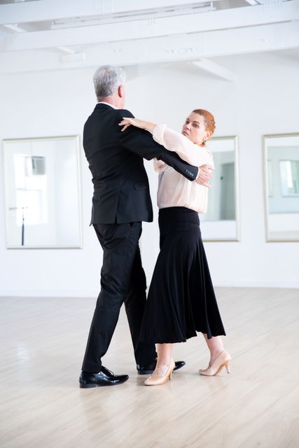 A happy elegant Caucasian senior couple spending time together in a ballroom, taking part in dancing class, dancing, holding hands and smiling. Active golden years hobby.