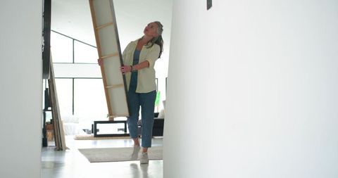 Woman carrying large canvas into bright modern living room for wall art installation